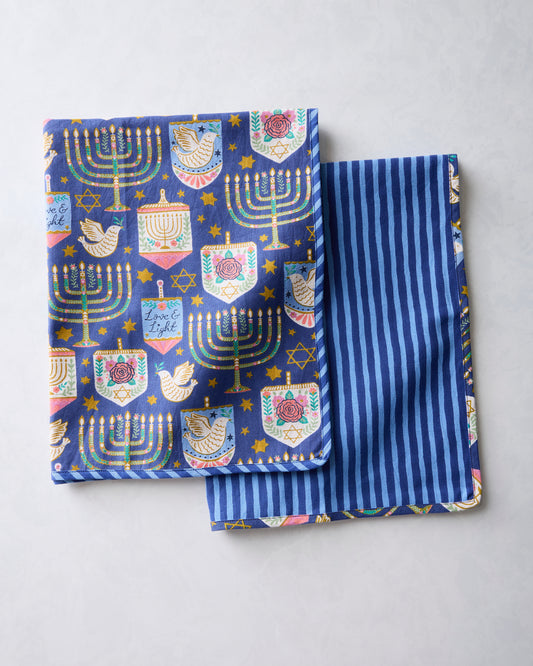 Two folded blue tea towels, one showing a Hanukkah symbol print and the other showing blue vertical stripes.