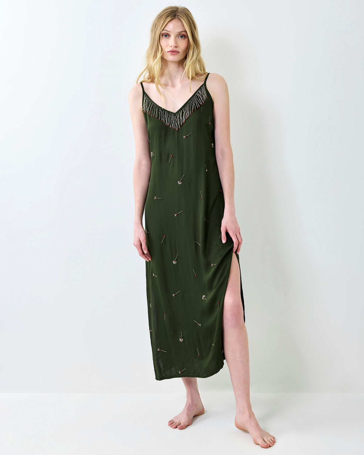 Full-length front view of an olive slip dress with a beaded fringe neckline, embroidered match motifs, and a side slit.
