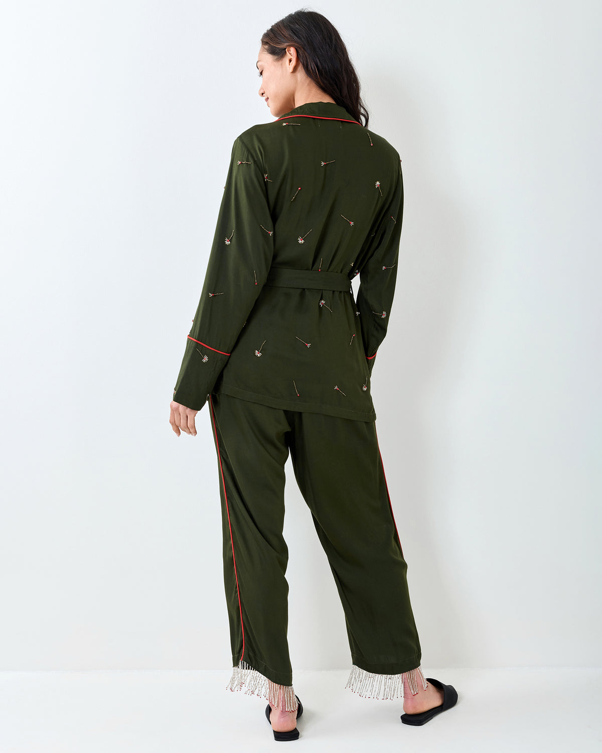 Back view of an olive long-sleeve top and matching pants with scattered embroidery, red piping, and beaded fringe at the pant cuffs.