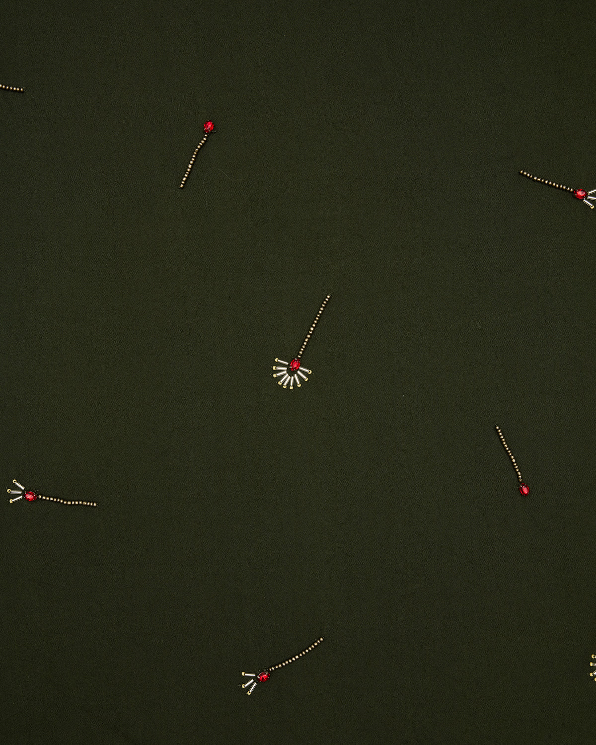 Close-up of the olive dress fabric with scattered embroidered match motifs and red bead details.