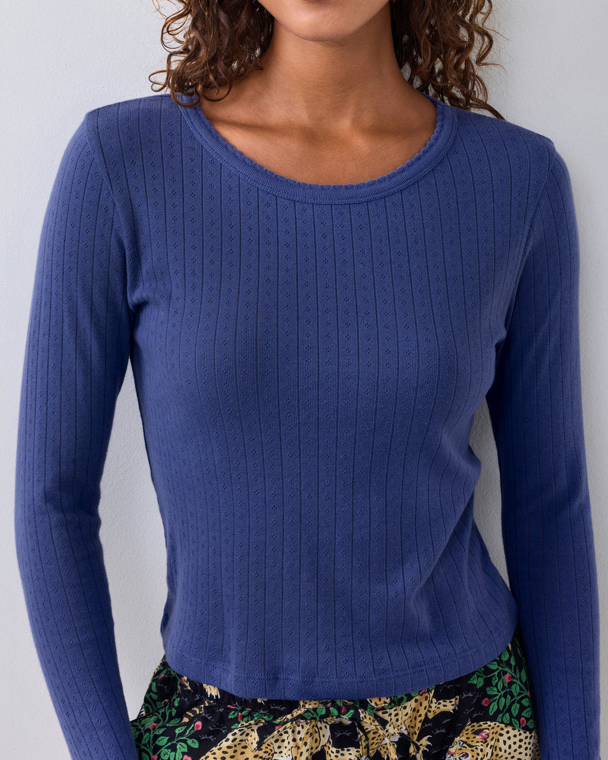 Blue long-sleeve pointelle top with a scalloped neckline, shown on a person with patterned pajama pants visible below.