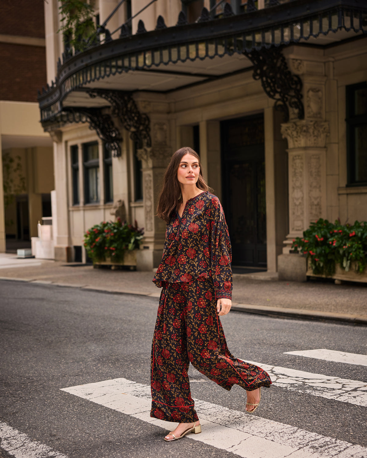 Person wearing a garnet floral blouse with full sleeves and matching wide-leg pants while crossing a street.