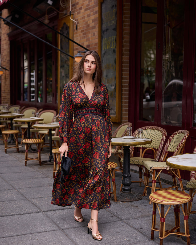 Full-length view of a person wearing a dark floral dress and sandals on a café sidewalk.