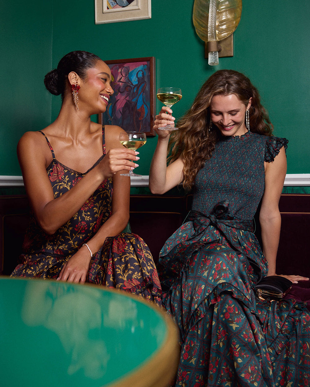 Model wearing the Nordic Garden Ready To Ruffle maxi dress seated beside another person, with both holding drinks.