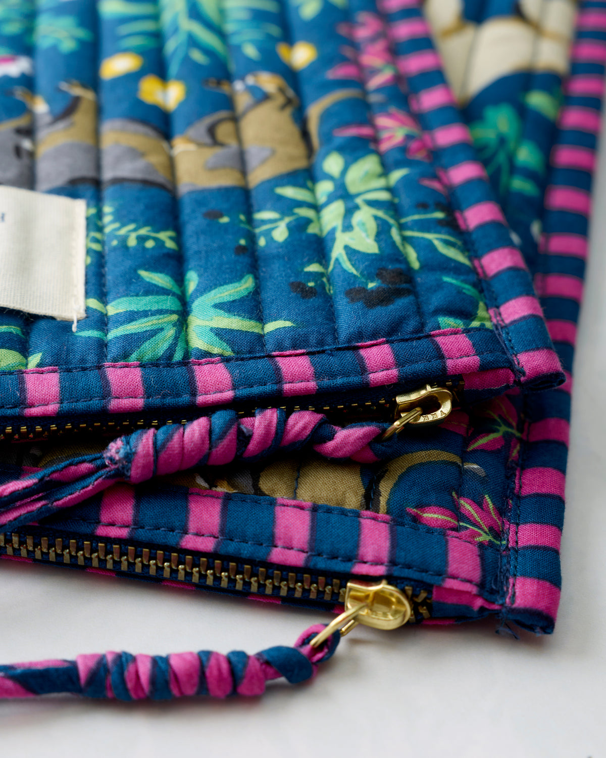 Close-up of the indigo pouch duo showing gold zipper hardware, zipper teeth, and a striped fabric pull.