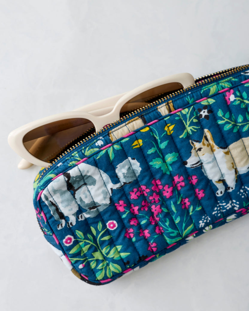 Quilted indigo zippered sunglasses case with floral and dog print, shown with sunglasses partially inserted.
