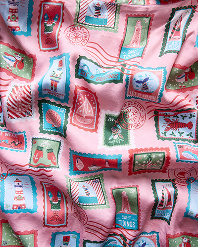 Close-up of pink fabric with a nautical holiday stamp print featuring shells, lighthouses, sailboats, stockings, and decorative lettering.