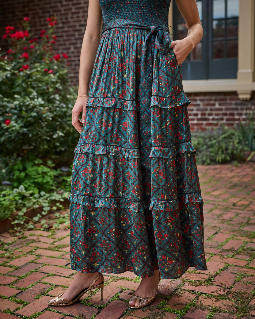 Close view of the Nordic Garden maxi dress showing its floral patterned fabric, tiered ruffles, tie waist, and side pockets.