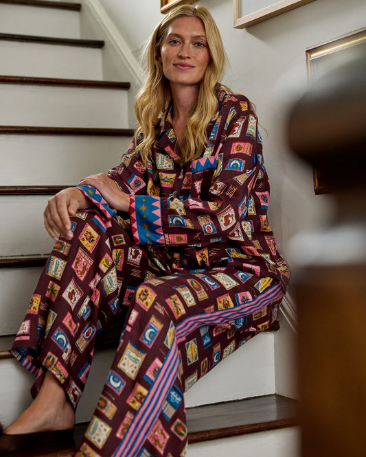 Seated view of the Cabernet Painted Matchbook pajama set, showing the notched-collar top, patterned cuffs, and wide-leg pants.