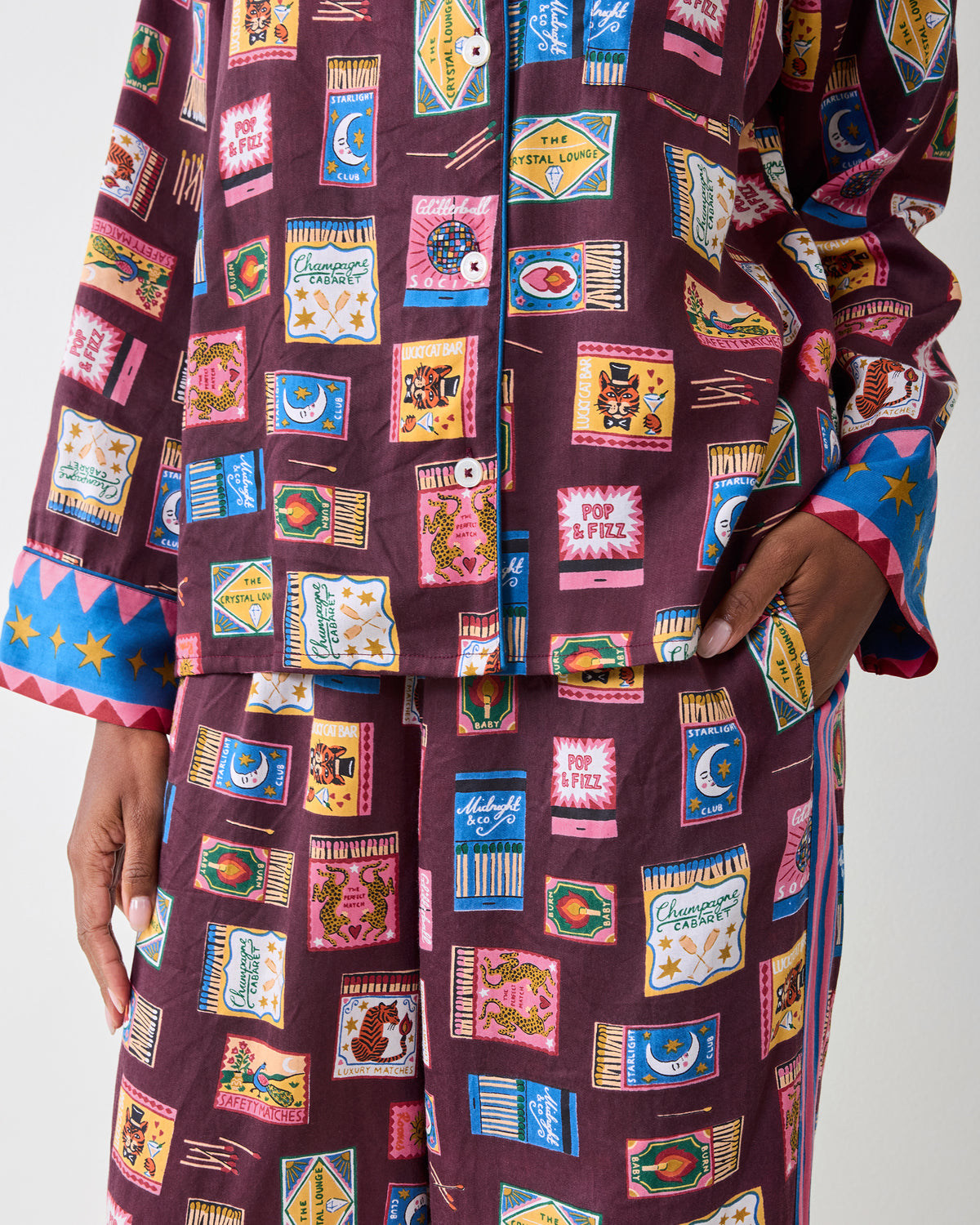 Close-up of the Cabernet Painted Matchbook pajama set showing the button-front top, matching pants, pocket, and multicolored matchbook print.