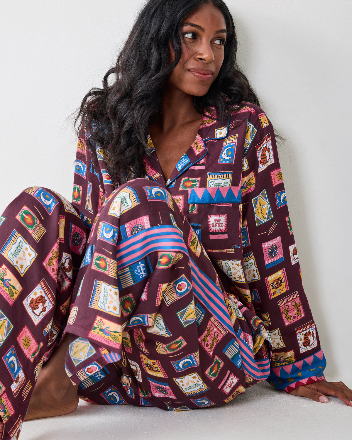 Person seated wearing the Painted Matchbook Cabernet pajama set, showing the patterned top, wide-leg pants, and striped pant detail.