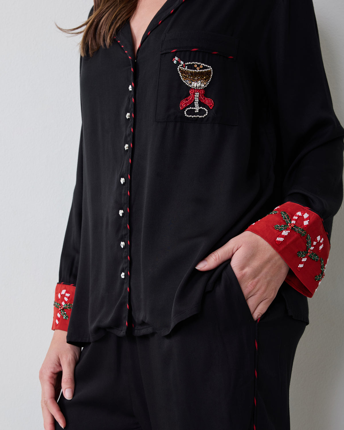 Close view of the black pajama shirt showing the chest pocket embroidery, red patterned cuffs, and button placket.