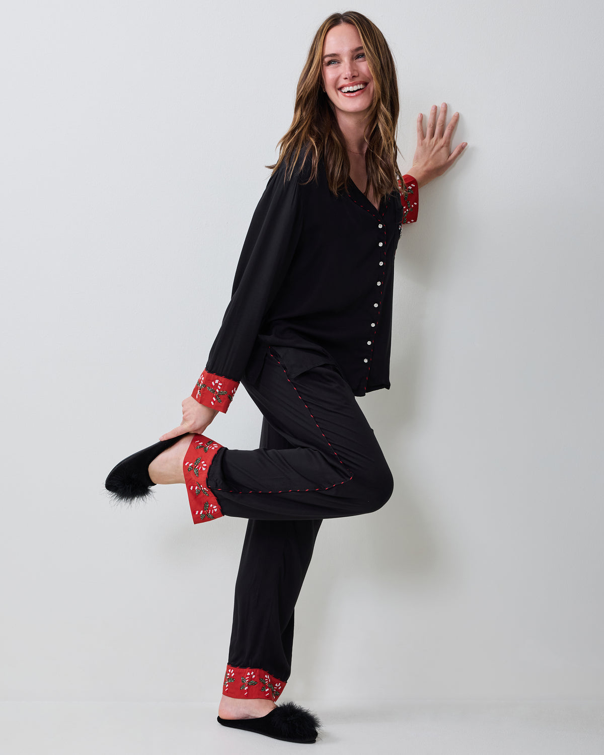 Person modeling the black pajama set in profile, showing the red patterned cuffs and pant hems with black slippers.
