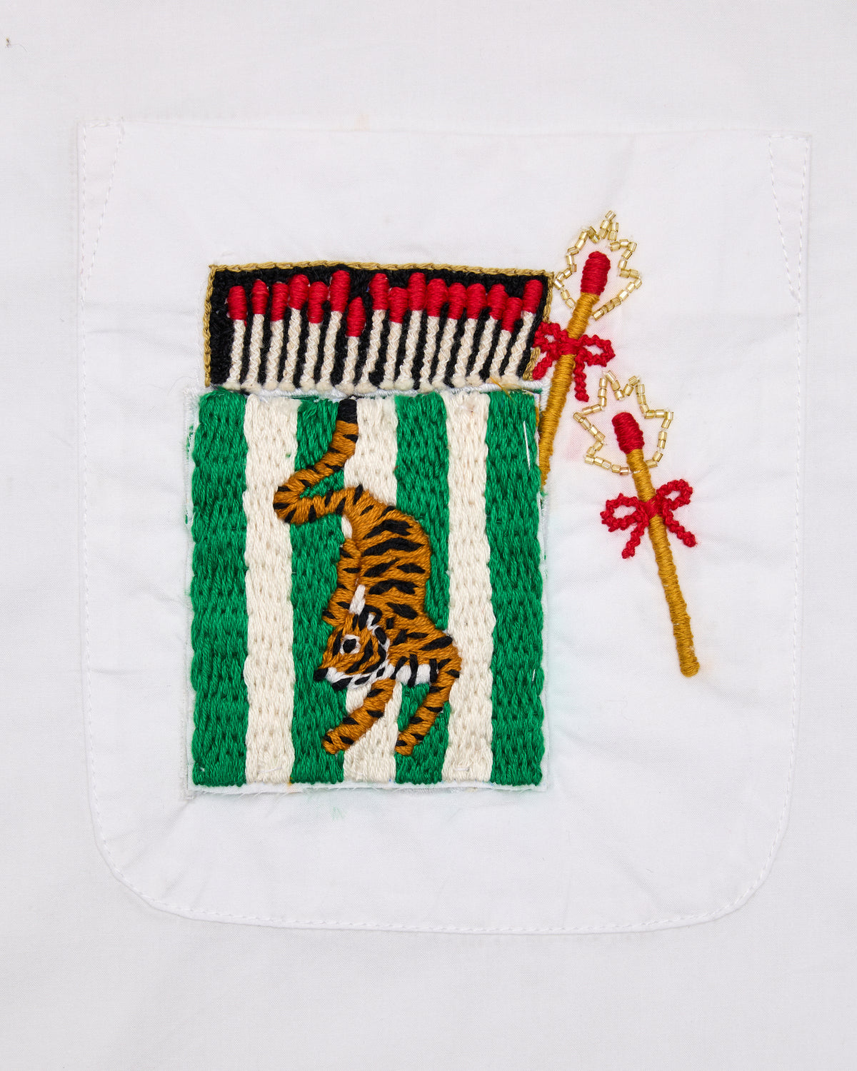 Close-up of the white shirt's chest pocket with an embroidered tiger between green stripes and matchstick motifs.