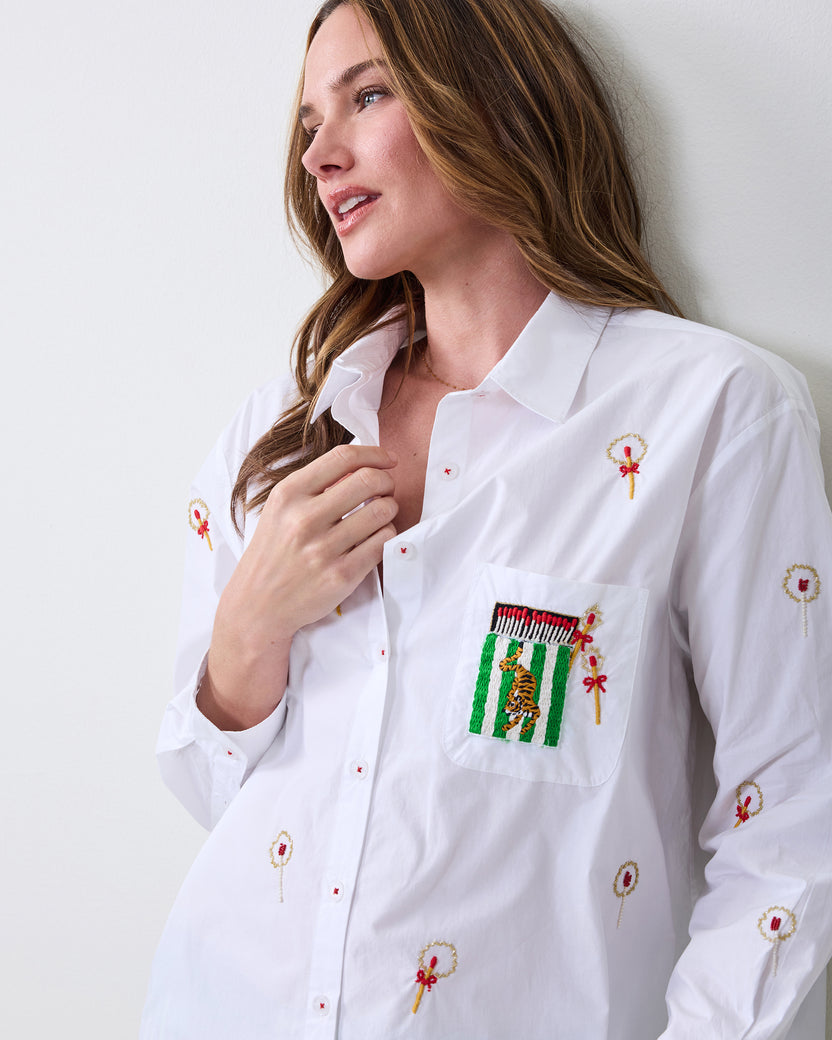 Close-up of the white button-down shirt showing embroidered matchstick motifs and a chest pocket with a striped tiger design.
