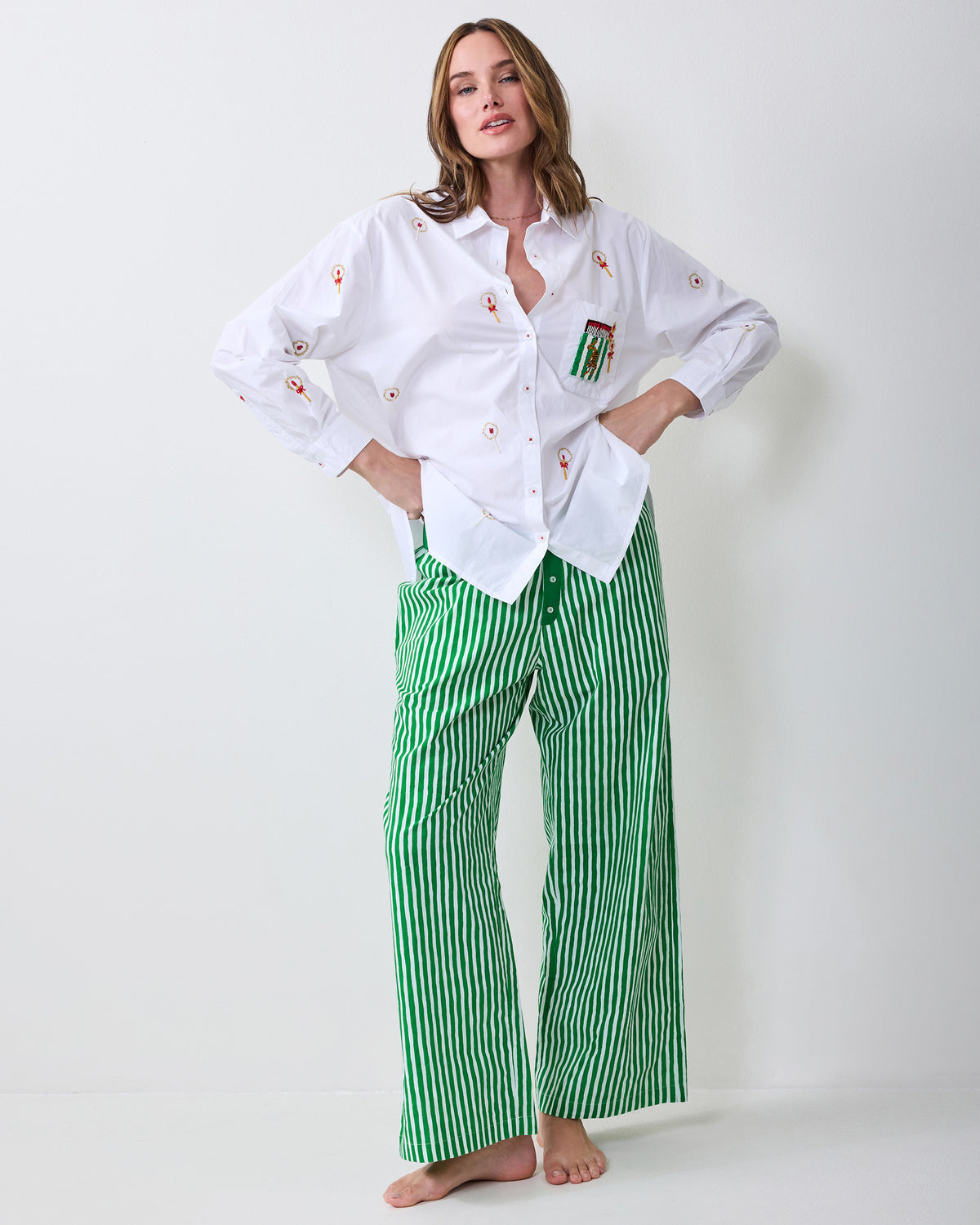 Model standing barefoot in a white embroidered button-down shirt and green-and-white striped pajama pants.