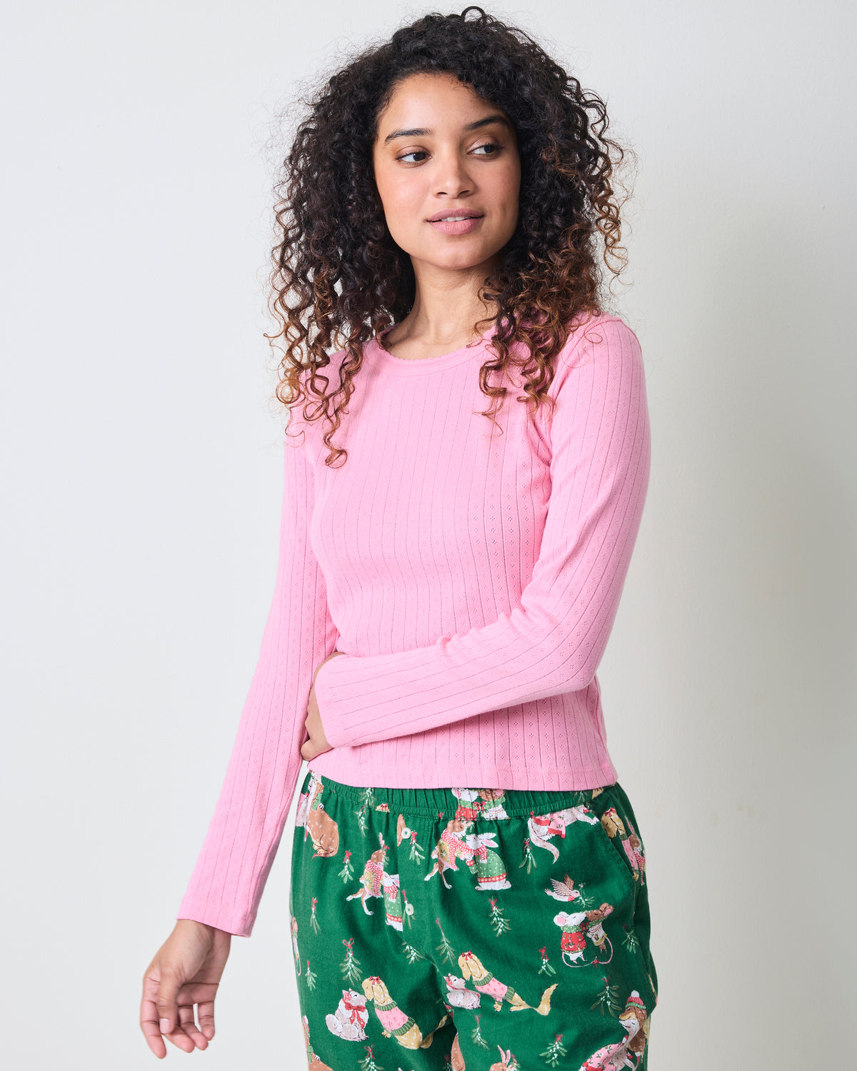Front three-quarter view of the pink taffy long-sleeve pointelle top with scalloped neckline, paired with green patterned pajama pants.