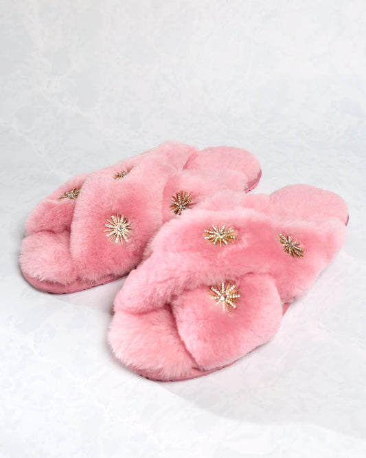 Pair of pink sheepskin slippers with rhinestone embellishments, shown at an angle.
