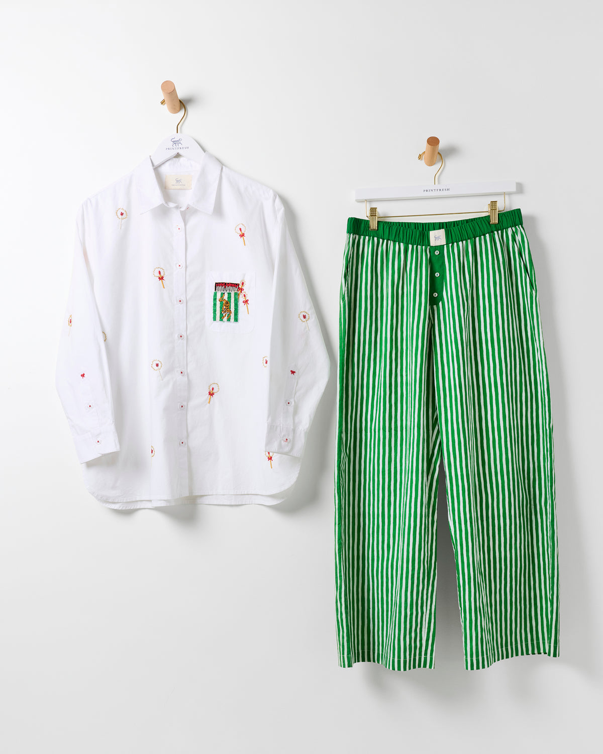 White embroidered button-down shirt and green-and-white striped pants hanging side by side.