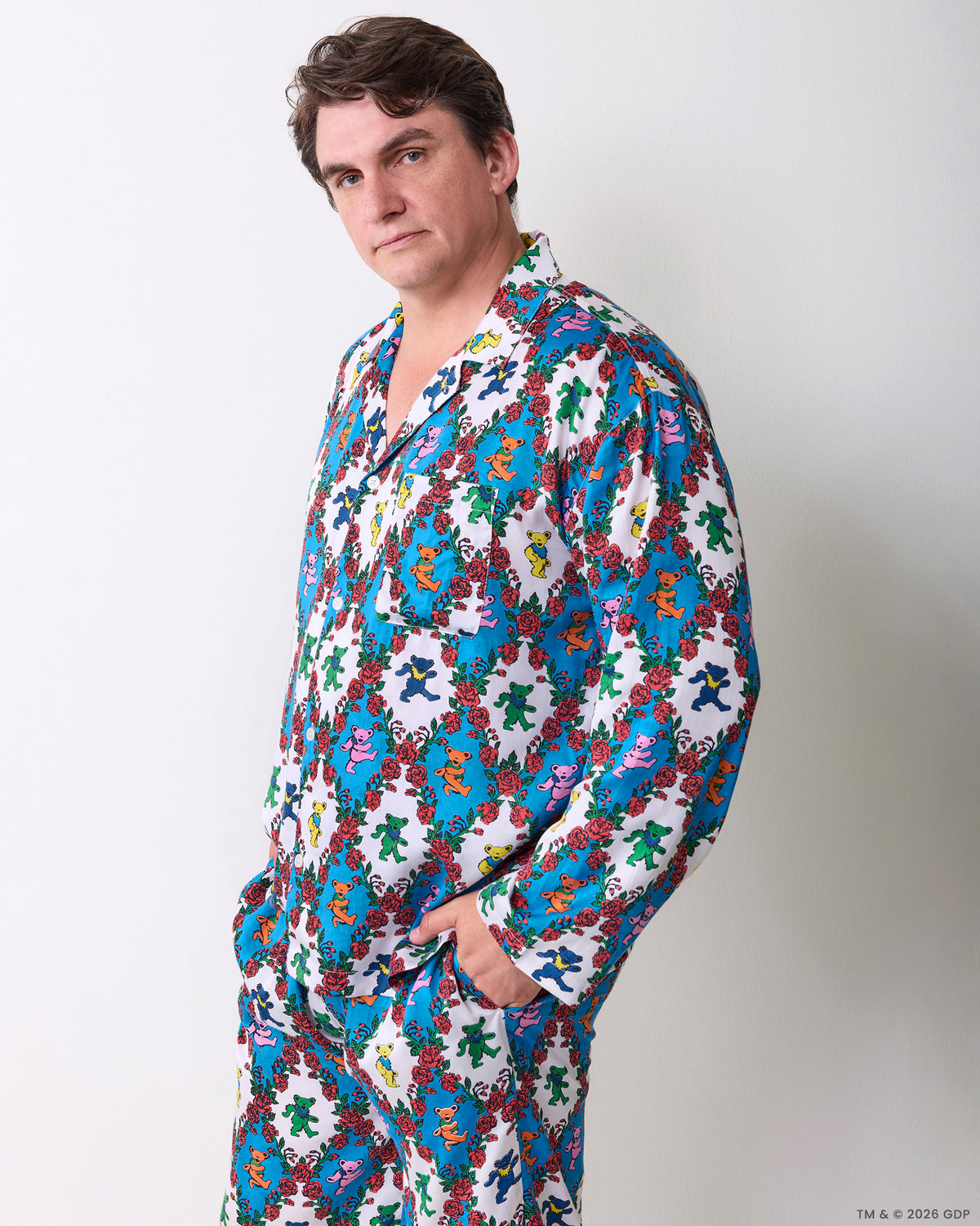 Three-quarter view of a person wearing the white long pajama set printed with colorful figures and red roses, with a chest pocket and side pockets.