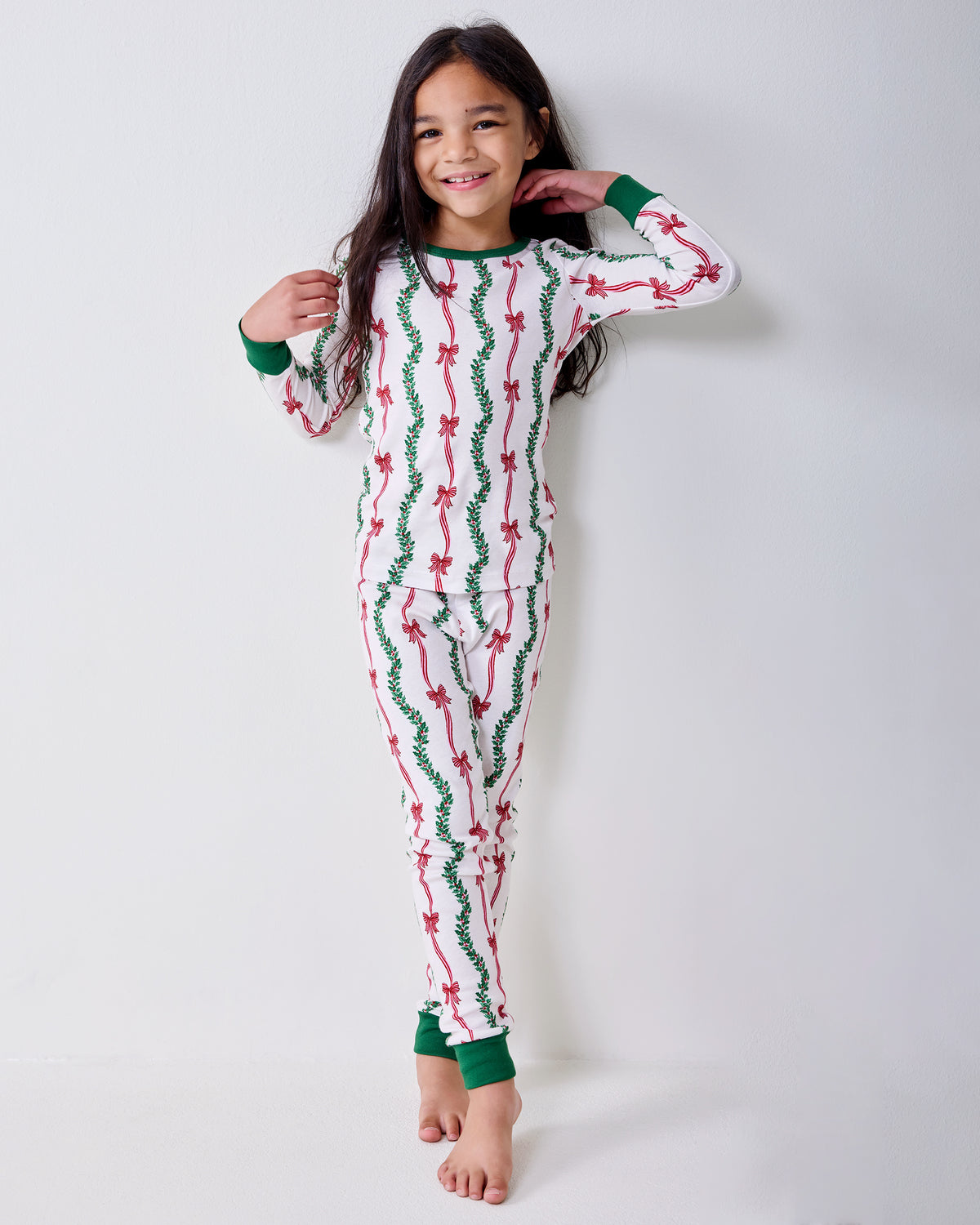 Front view of a child wearing the Ribbons & Bows long pajama set with green cuffs and pink bow and garland print.