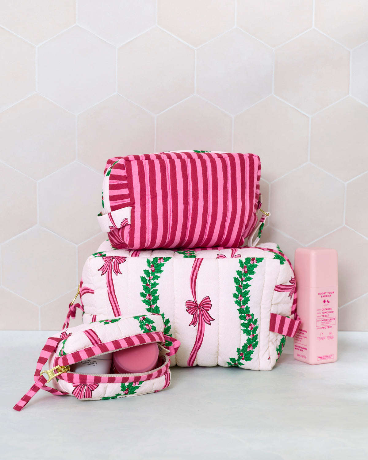 Three quilted pouches in the Ribbons & Bows print, stacked beside an open pouch and a pink bottle.