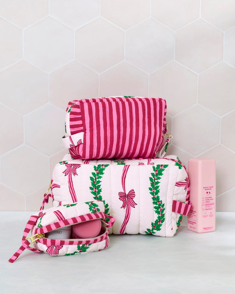 Three quilted pouches in the Ribbons & Bows print, stacked beside an open pouch and a pink bottle.