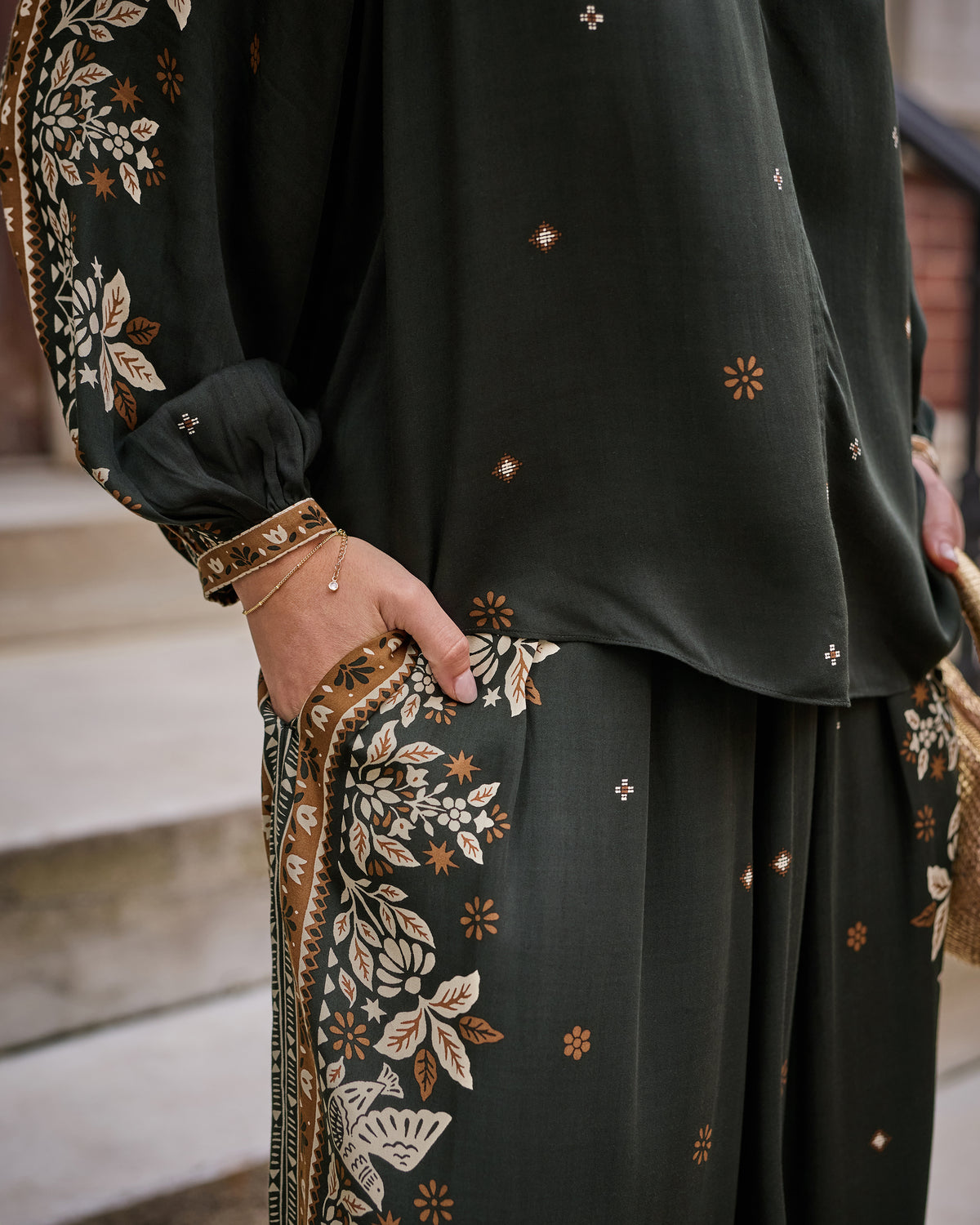 Close-up of the dark green blouse sleeve and matching pants pocket, showing floral patterned panels and small scattered motifs.