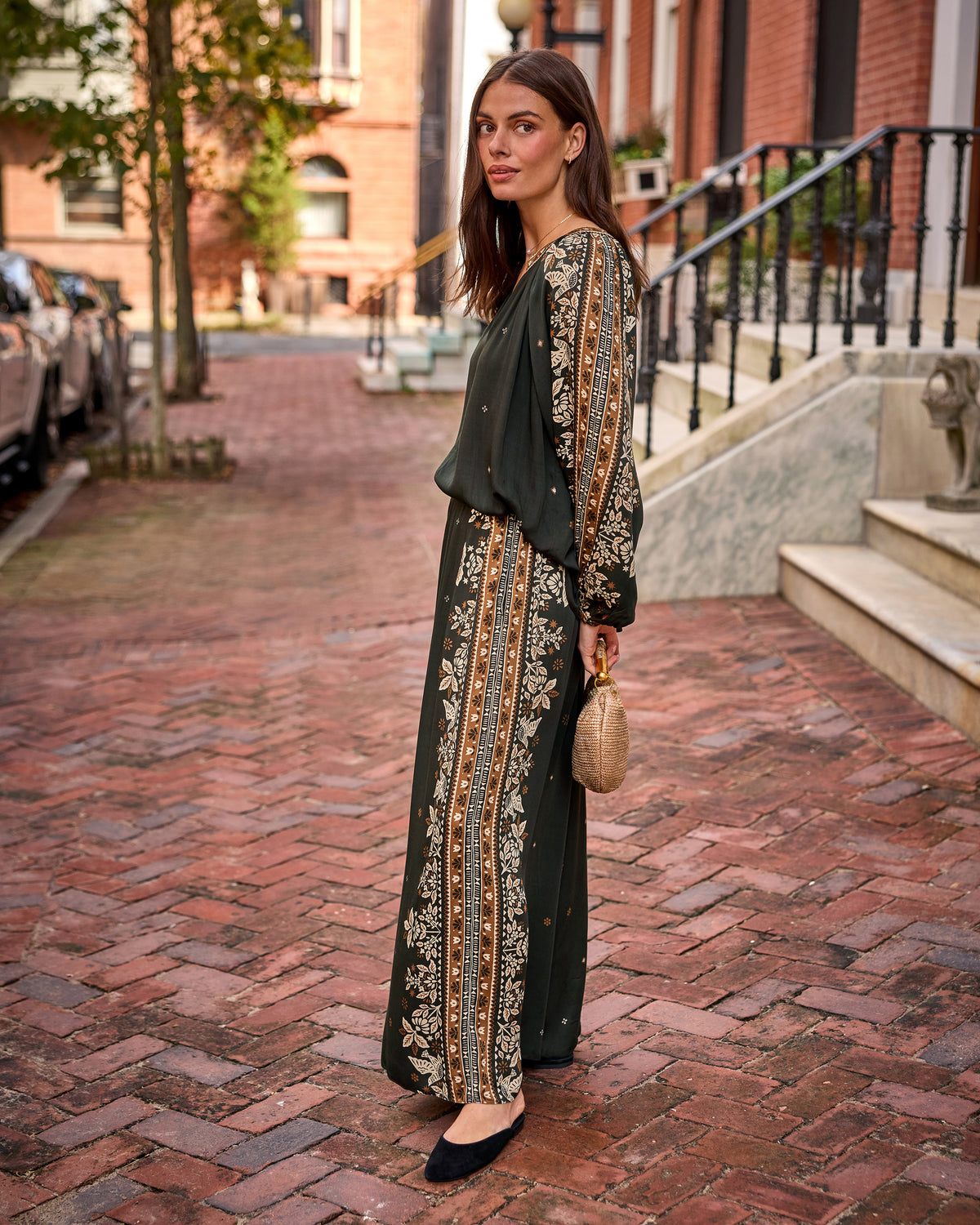 Three-quarter view of the Sasha Pants in dark green with long floral patterned side panels, worn on a brick sidewalk.