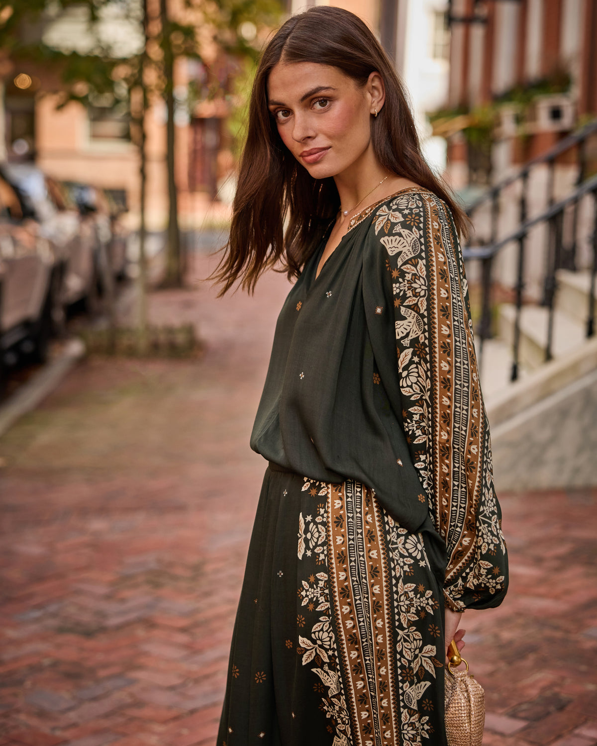 Three-quarter view of the Hallie Blouse and Sasha Pants in dark green with coordinated floral patterned side panels, worn on a brick sidewalk.