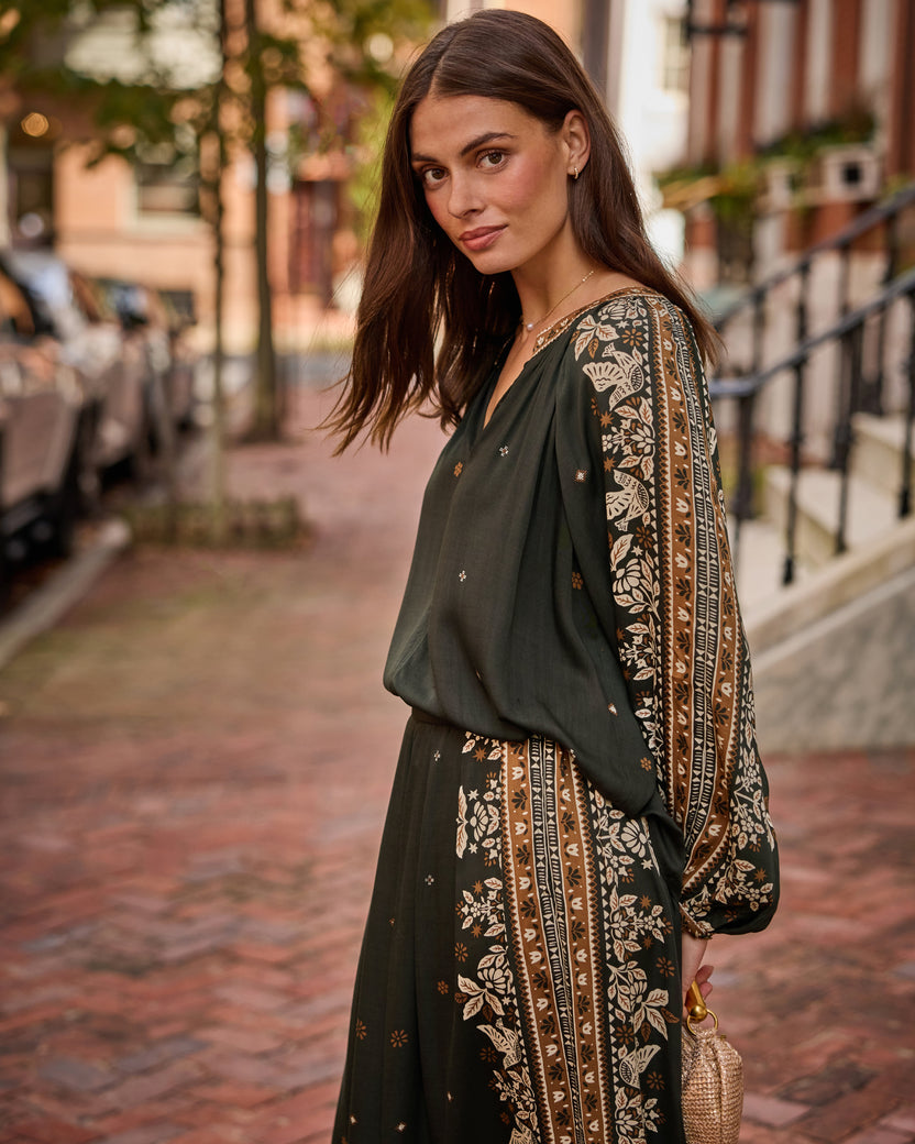 Three-quarter view of the Hallie Blouse and Sasha Pants in dark green with coordinated floral patterned side panels, worn on a brick sidewalk.