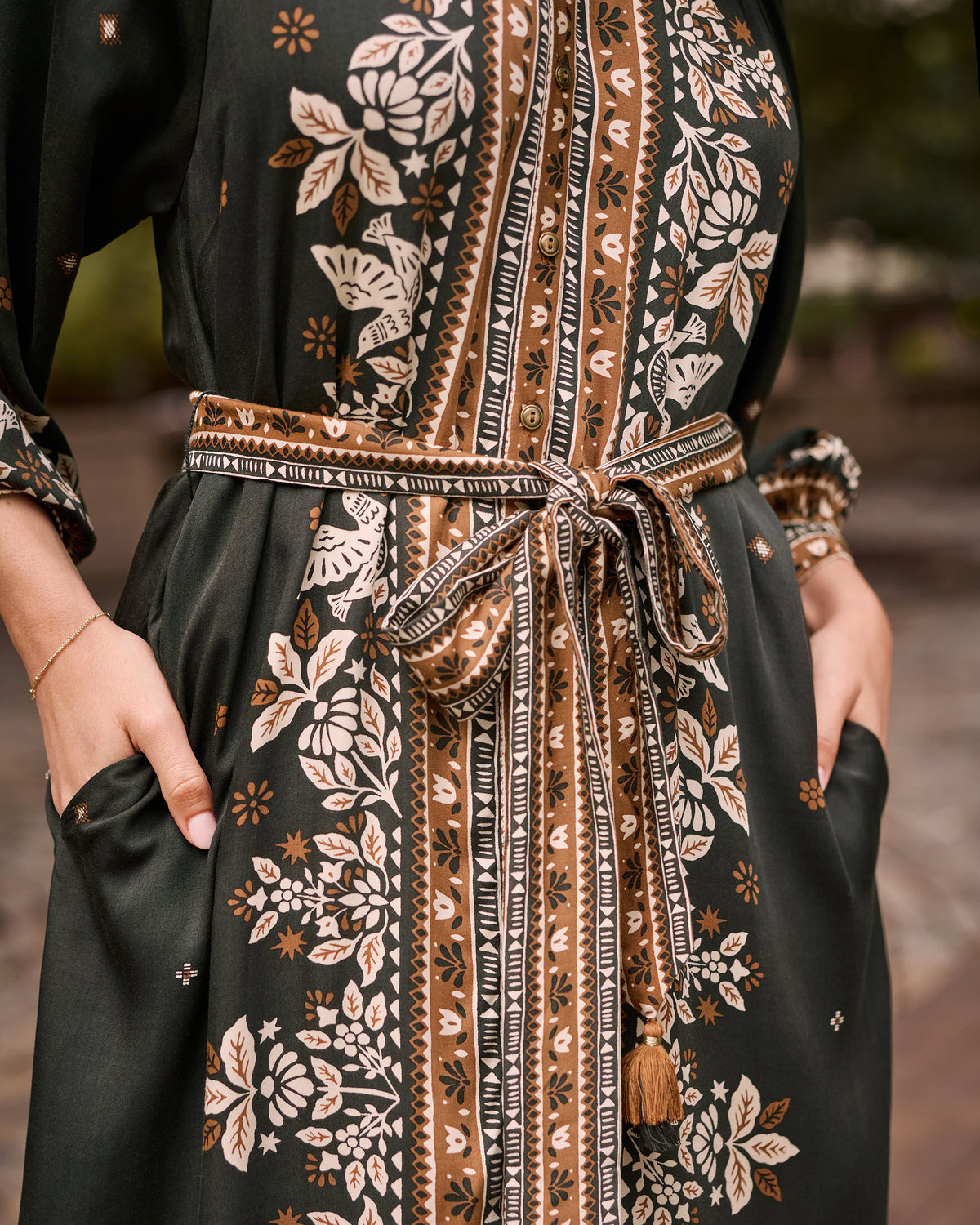 Close-up of the Solstice Tapestry Hunter dress showing its patterned neckline and center panel, tie belt with tassels, and side pocket.