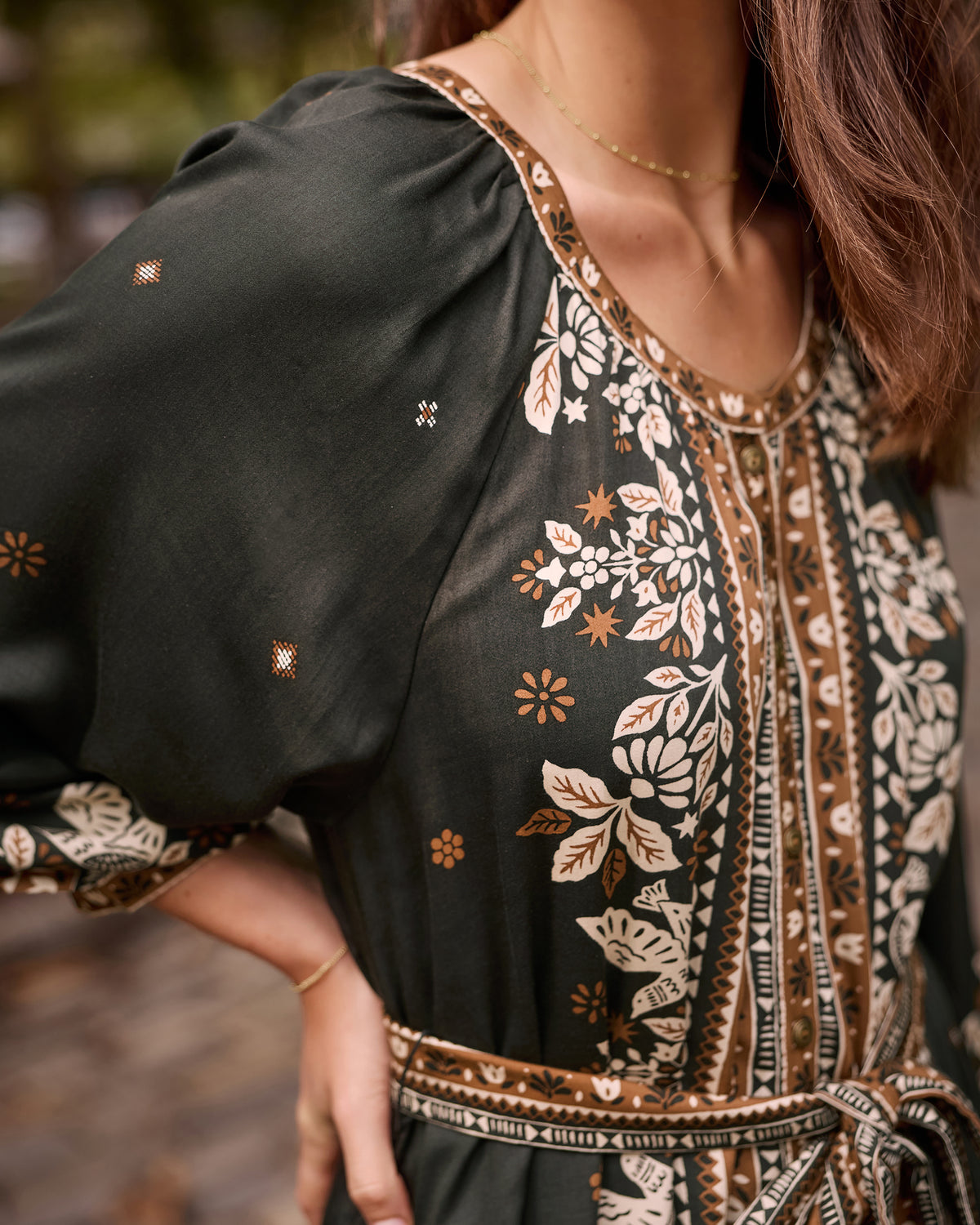 Close-up of the Solstice Tapestry Hunter dress showing the gathered shoulder, loose sleeve, patterned neckline, and tie waist.