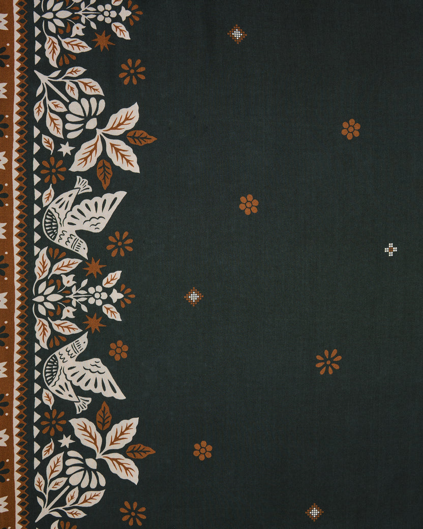 Close-up swatch of the Solstice Tapestry print with floral border motifs, geometric stripes, and small scattered flowers on a dark green background.