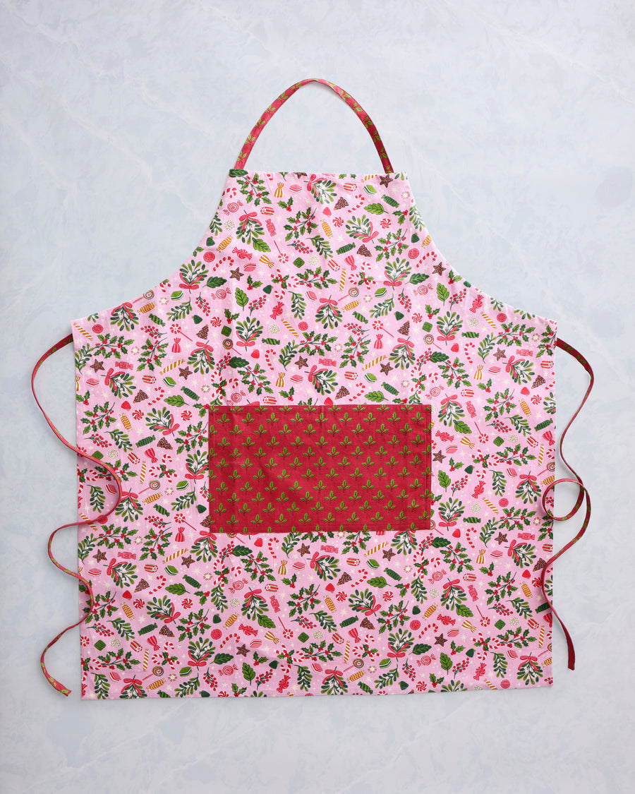 Candy pink apron with a colorful holiday candy and foliage print, front pocket, neck loop, and side ties.