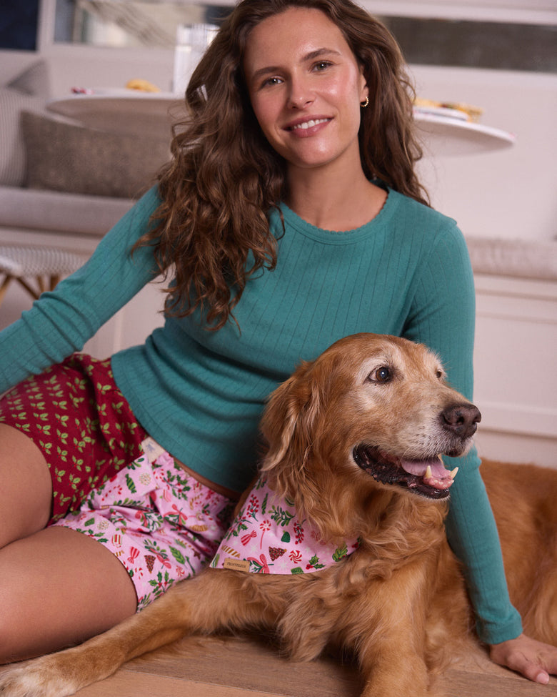 Lifestyle view of the Sweet Tooth Boyfriend Boxer in Candy Pink, with a person wearing the printed shorts beside a dog wearing a matching patterned bandana.