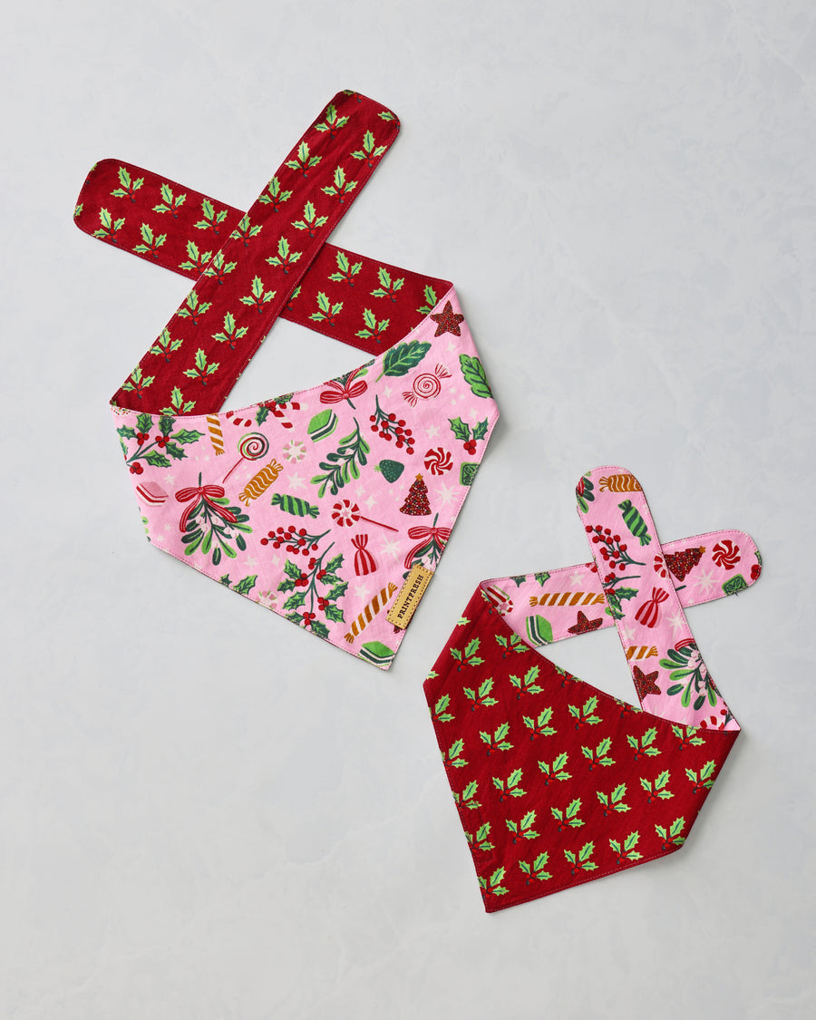 Two pet bandanas laid flat, showing pink candy motifs and red holly patterns.