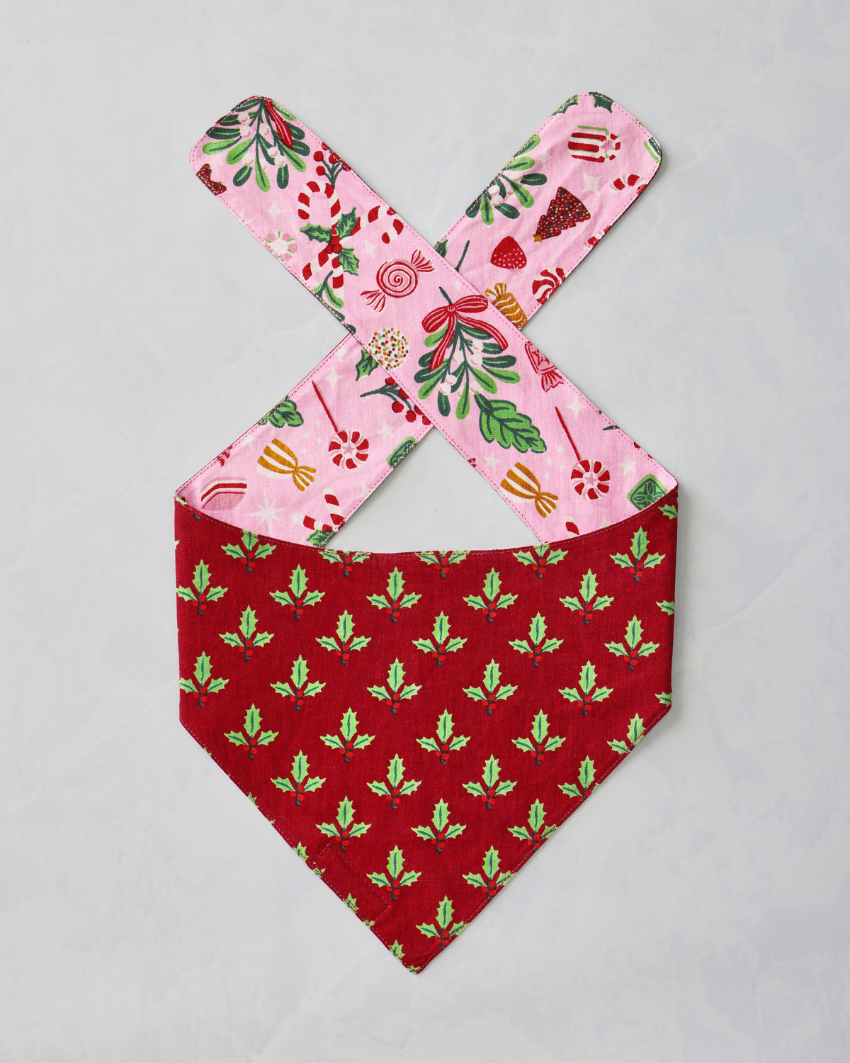 Pet bandana laid flat with a red holly-patterned body and pink patterned ties.