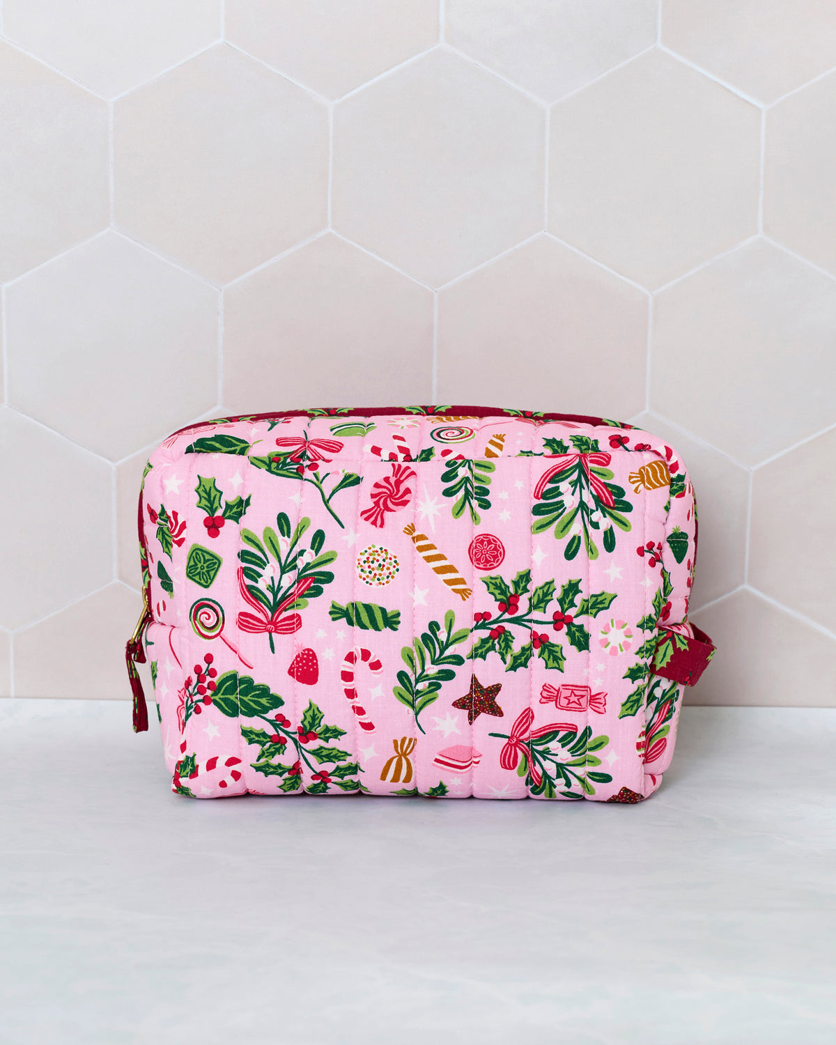 Candy pink quilted pouch with a colorful holiday candy, holly, and foliage print, shown upright from the front.
