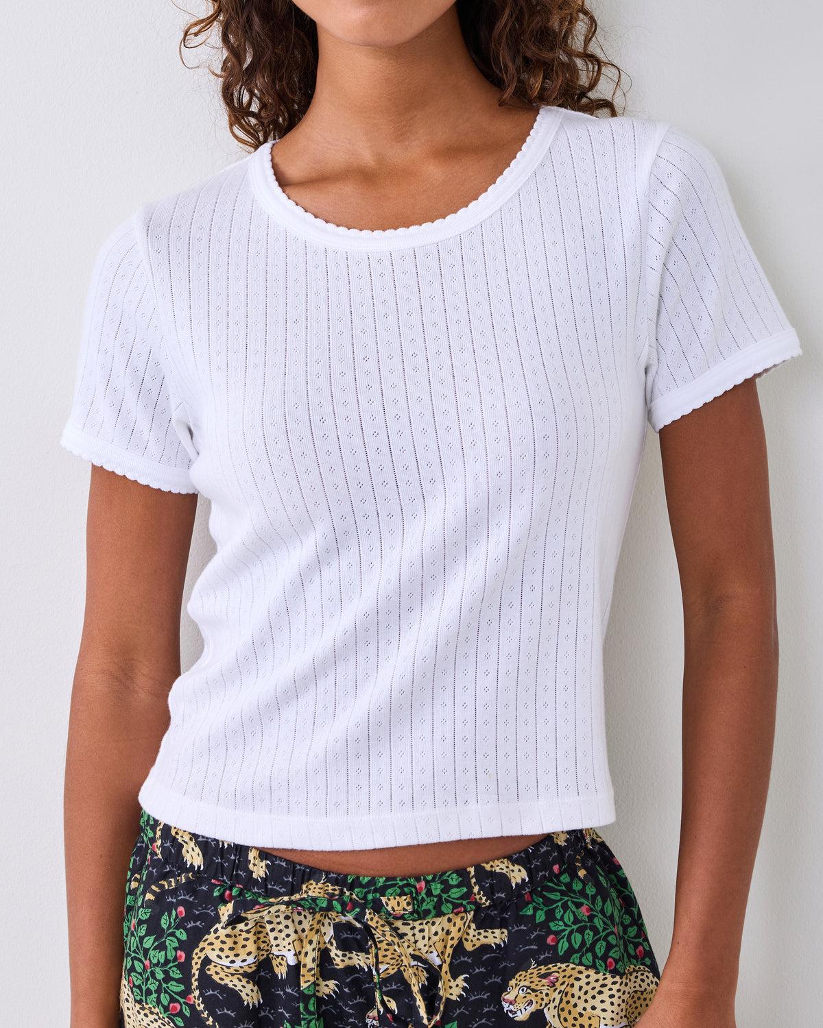 White short-sleeve pointelle top with scalloped neckline and sleeve edges, shown on a person.