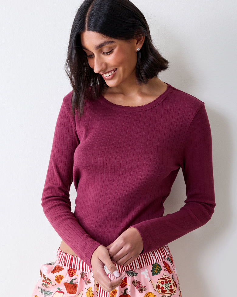 Three-quarter front view of a wine-colored long-sleeve pointelle top with a scalloped neckline and vertical eyelet pattern.