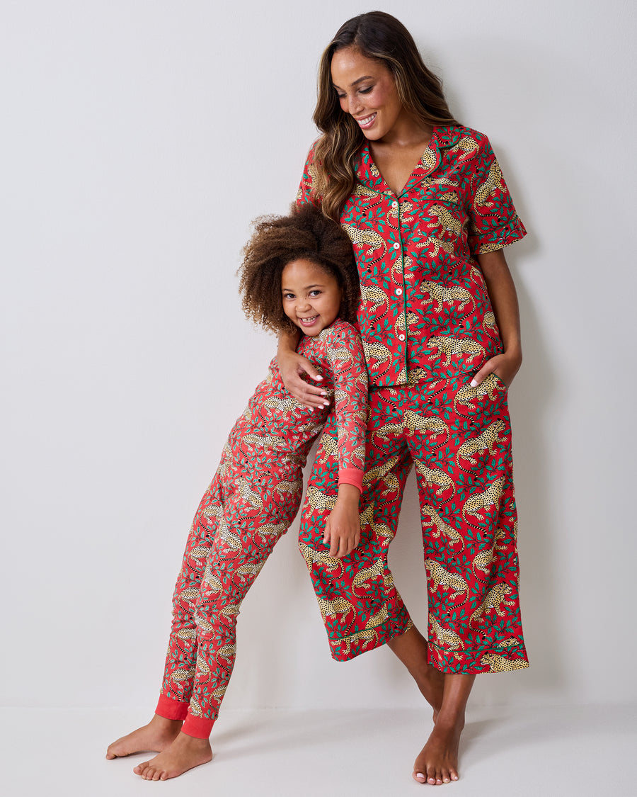 Adult and child wearing matching ruby short-sleeve pajama sets with a leopard-and-holly print.