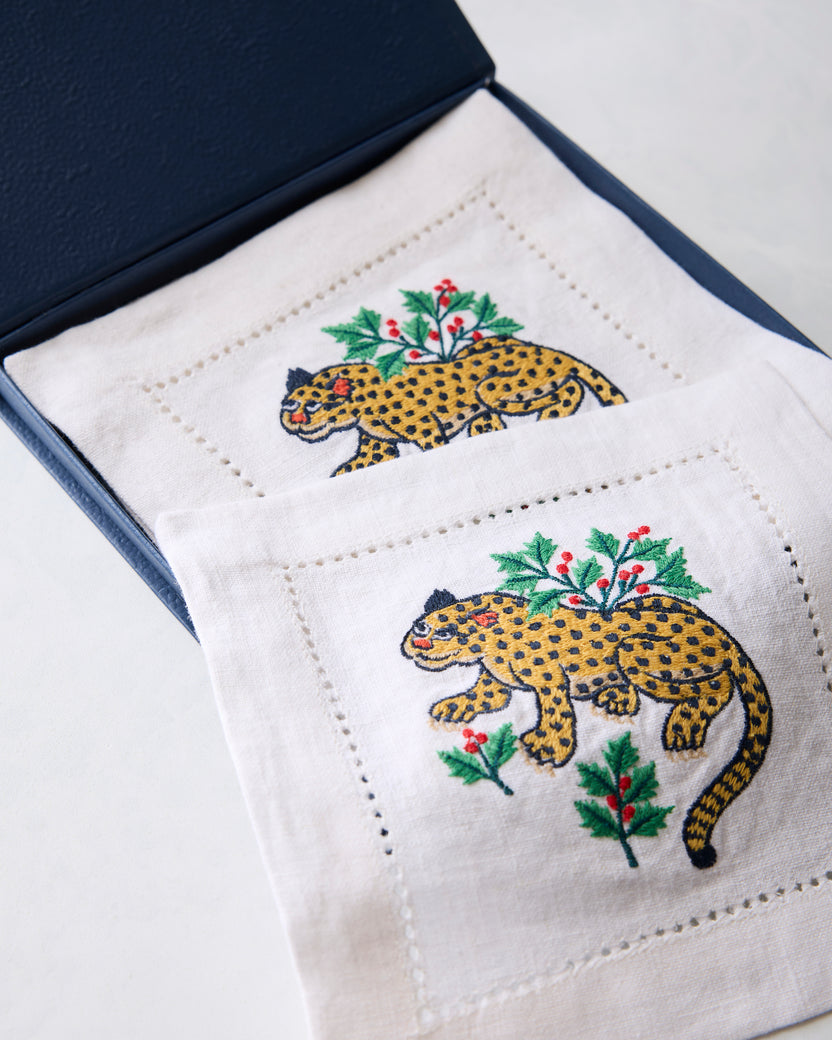 Open blue box displaying Winter Holly Bagheera embroidered cocktail napkins with spotted cats and holly branches.