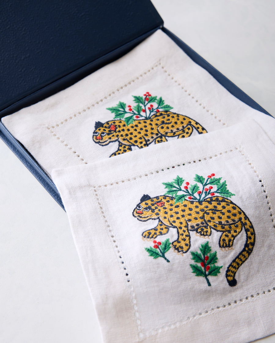 Open blue box displaying Winter Holly Bagheera embroidered cocktail napkins with spotted cats and holly branches.