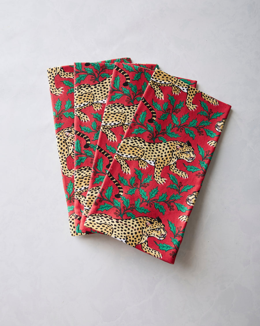 Four folded ruby dinner napkins with leopard and holly print arranged in an overlapping stack.