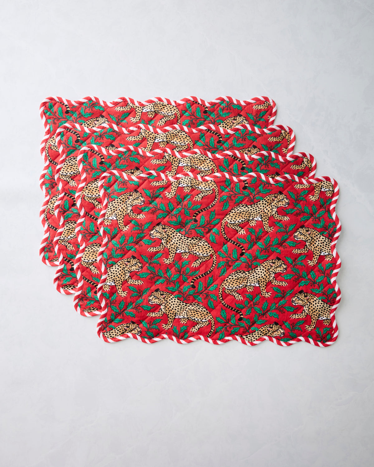 Set of four Winter Holly Bagheera placemats stacked together, with scalloped edges and a red leopard-and-holly print.