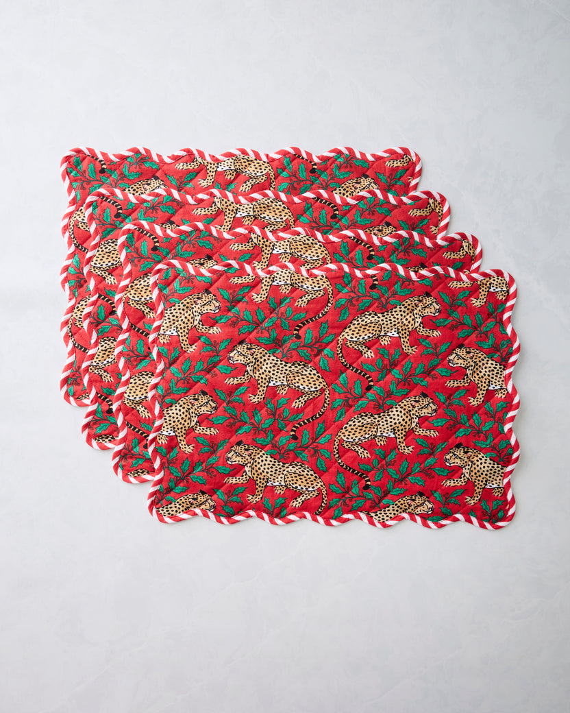 Set of four Winter Holly Bagheera placemats stacked together, with scalloped edges and a red leopard-and-holly print.