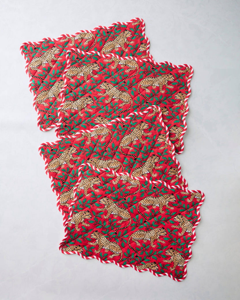 Four Winter Holly Bagheera placemats overlapped in a diagonal arrangement, showing scalloped edges and a red leopard-and-holly print.