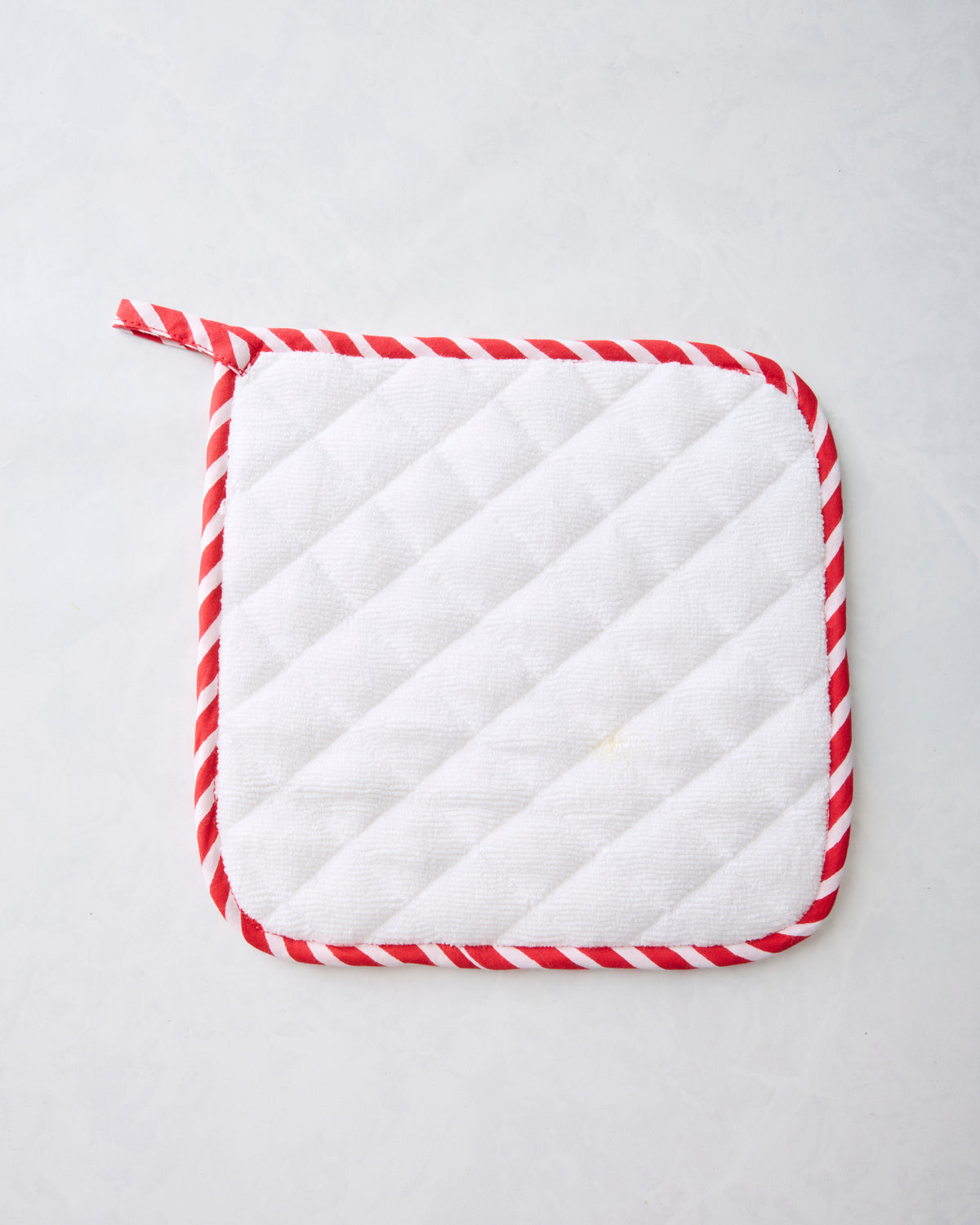 Back of a ruby pot holder showing white quilted padding and red-and-white striped trim.