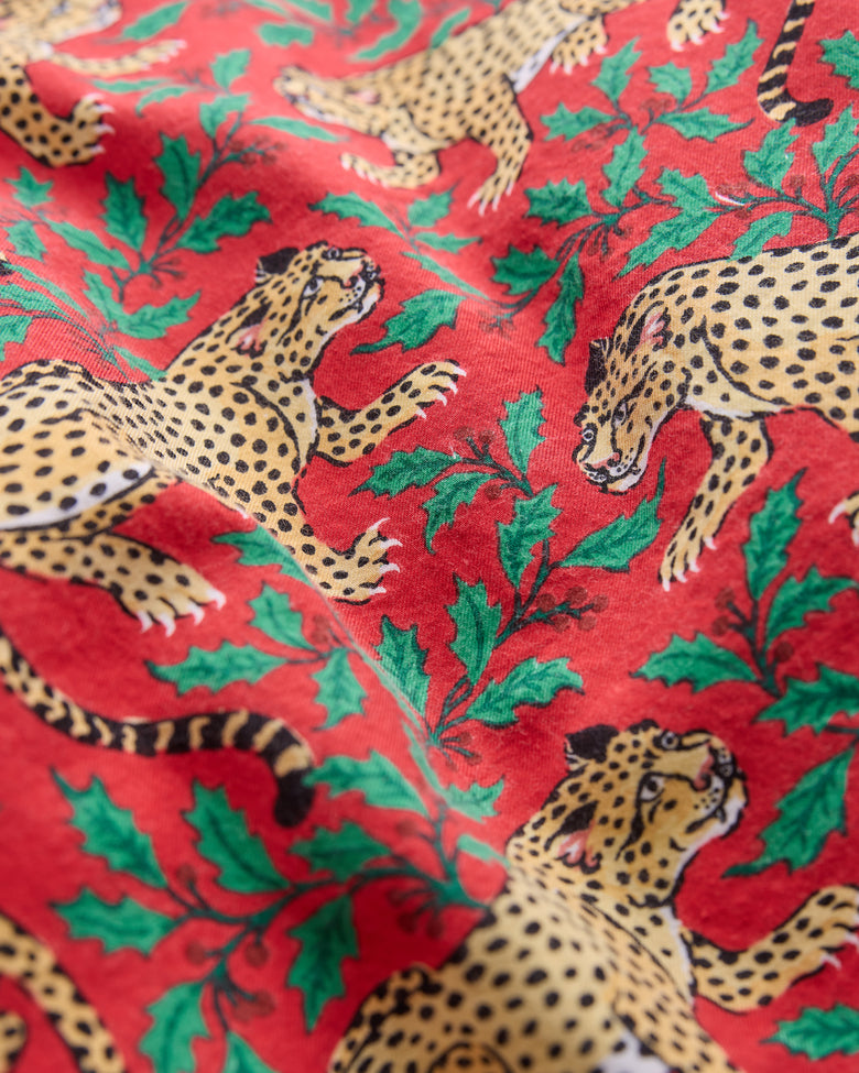 Close-up of red pajama fabric printed with spotted leopards and green holly leaves.